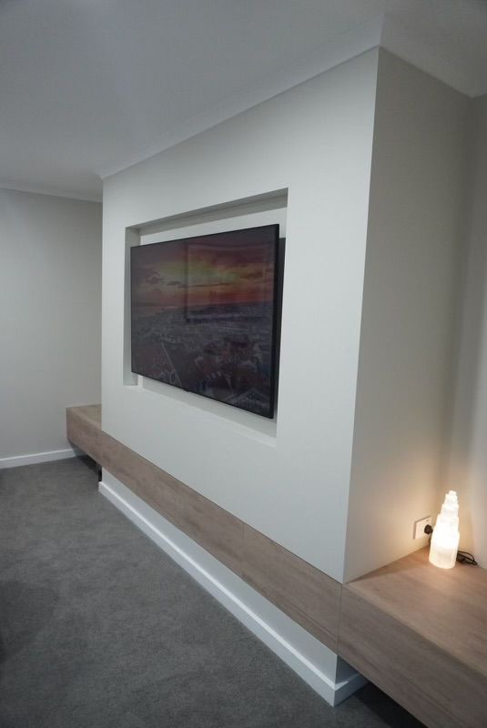 Modern living room with TV embedded in white wall. Long wooden shelf below, with a small lamp. — Hallam & Sons in Beard, ACT