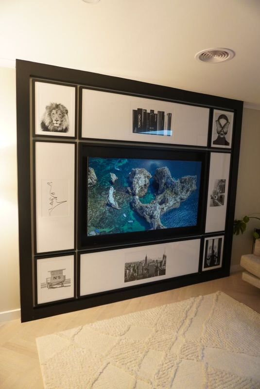 A large TV screen framed with black trim and surrounded by framed black and white pictures, set against a white wall. — Hallam & Sons in Beard, ACT