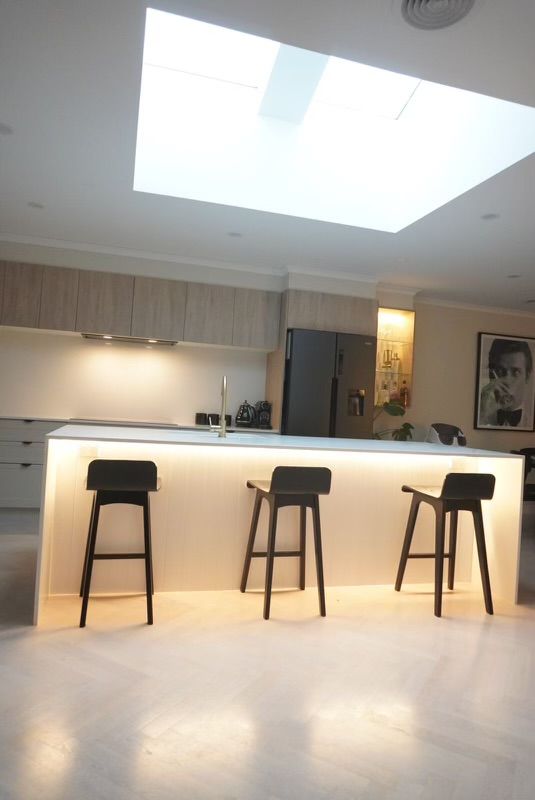 Modern kitchen with an illuminated island and three black stools. Skylight overhead. — Hallam & Sons in Beard, ACT