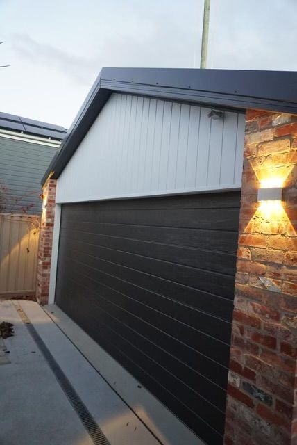 Black garage door, white upper wall, brick sides with lights. Grey roof and driveway. — Hallam & Sons in Beard, ACT