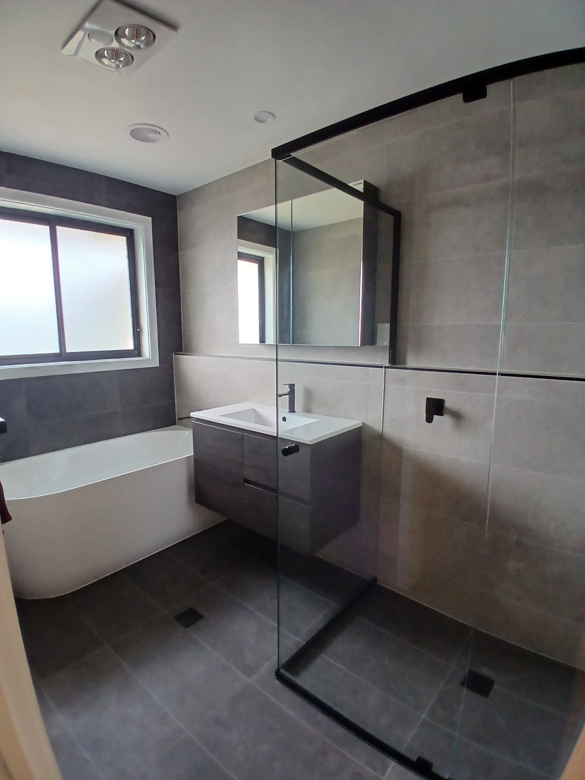 Modern bathroom with gray tiles, a floating vanity, glass shower enclosure, and bathtub. — Hallam & Sons in Beard, ACT