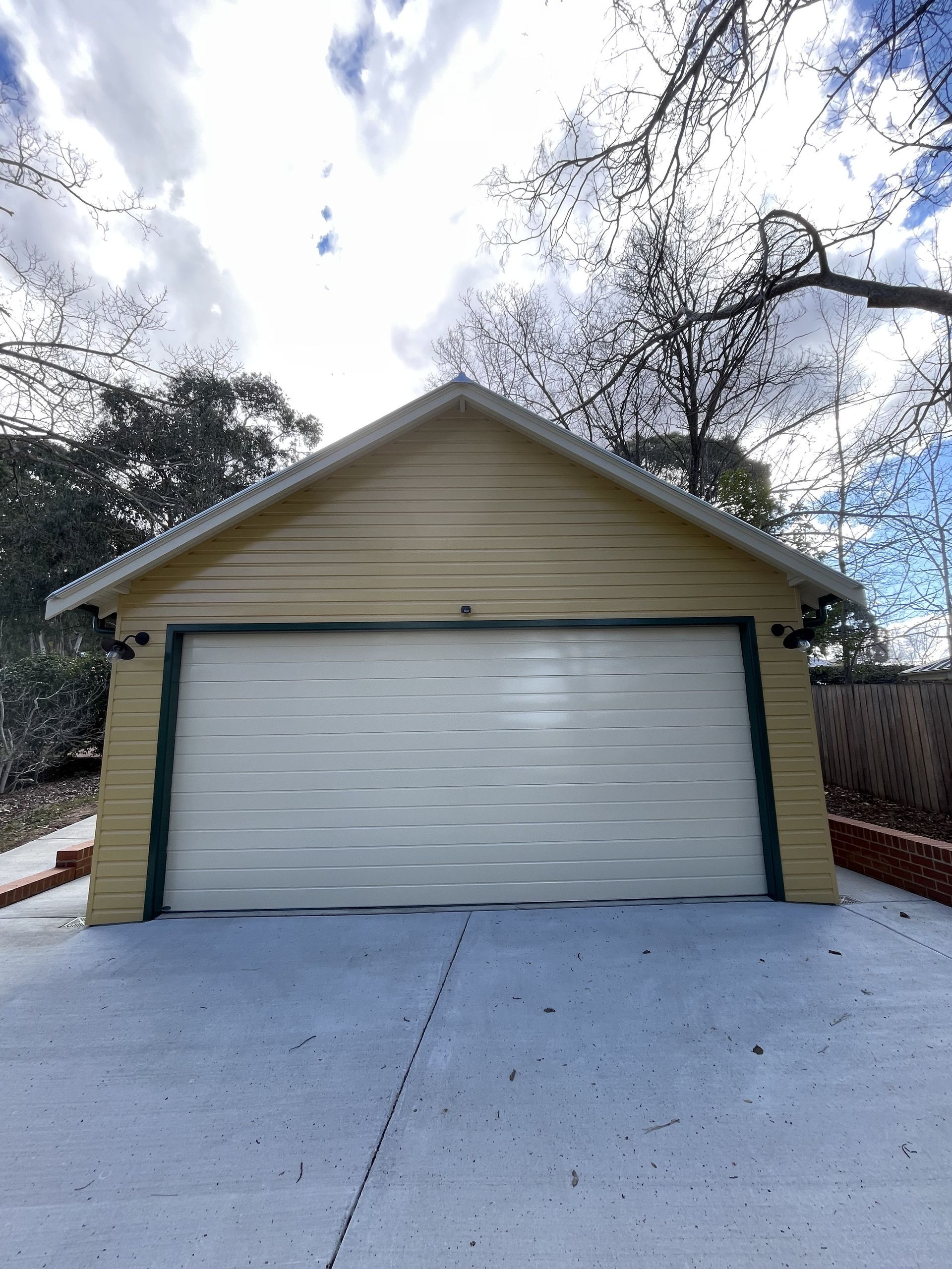 Yellow garage with white garage door on a concrete driveway, under a cloudy sky. — Hallam & Sons in Beard, ACT