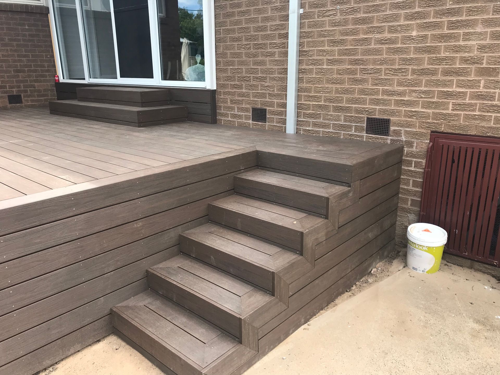 Composite deck with steps against a brick wall, leading to a sliding glass door. — Hallam & Sons in Beard, ACT