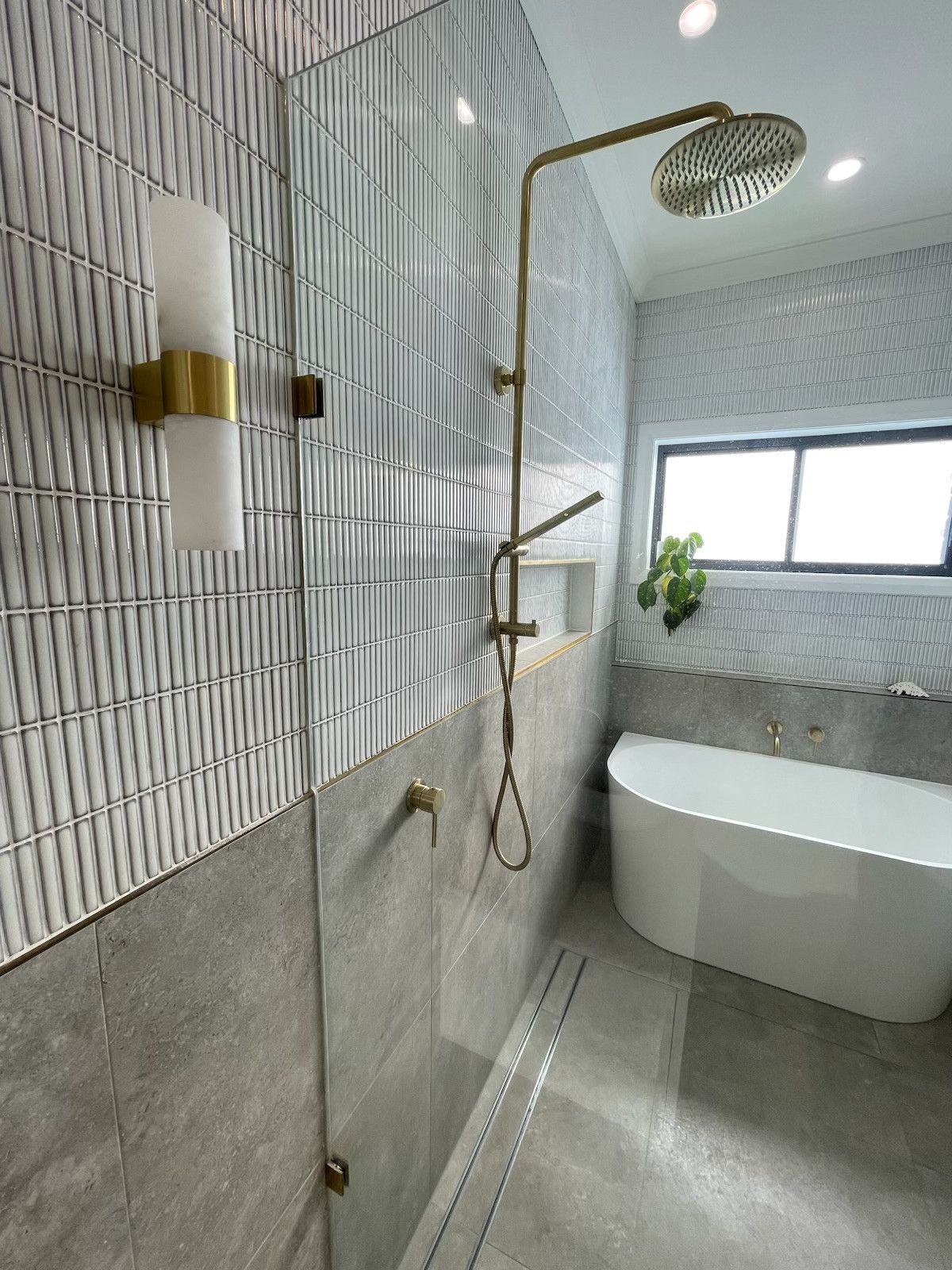 Modern bathroom with patterned gray tile, gold shower fixtures, and a freestanding tub. — Hallam & Sons in Beard, ACT