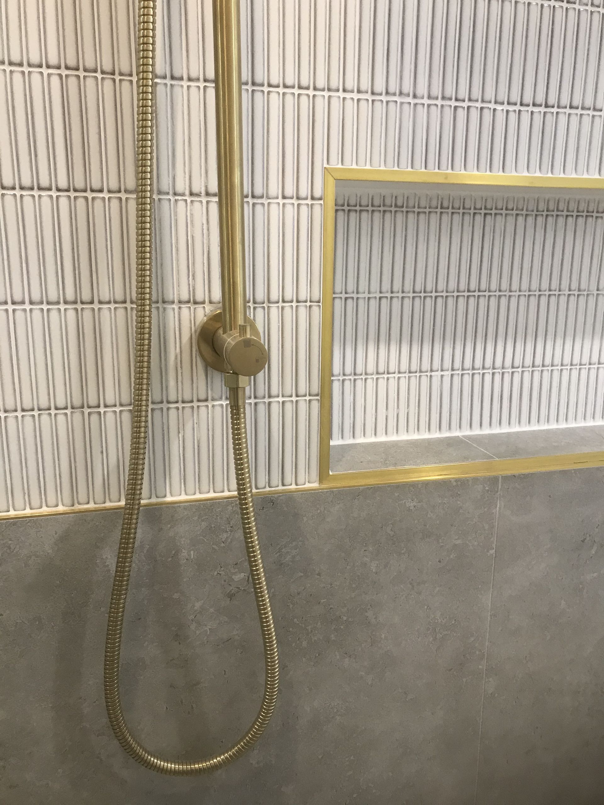 Gold shower fixtures against white and gray tiled wall with recessed shelf. — Hallam & Sons in Beard, ACT