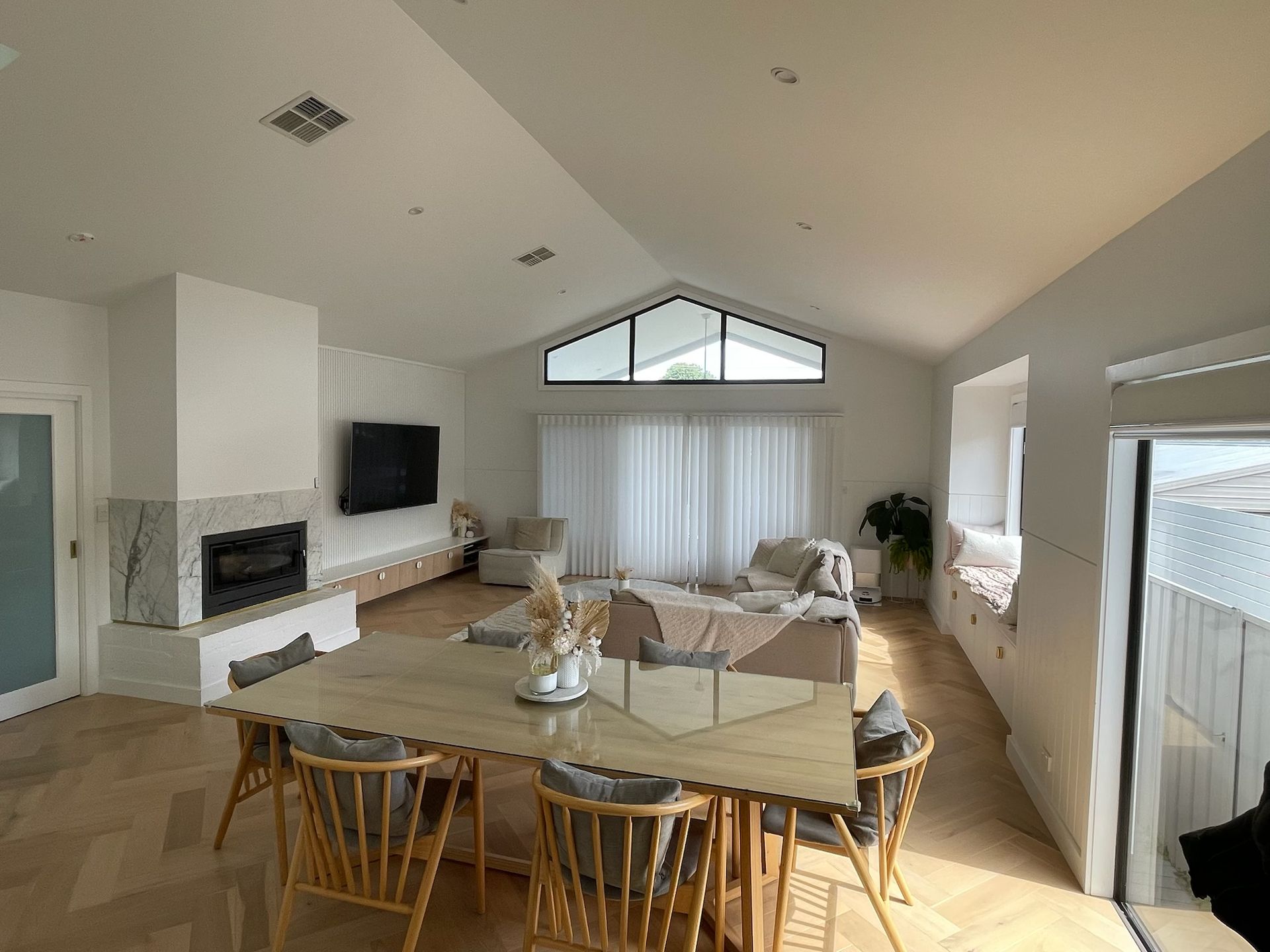 Bright, open living room with dining table, fireplace, and arched window. Cream and light wood tones. — Hallam & Sons in Beard, ACT
