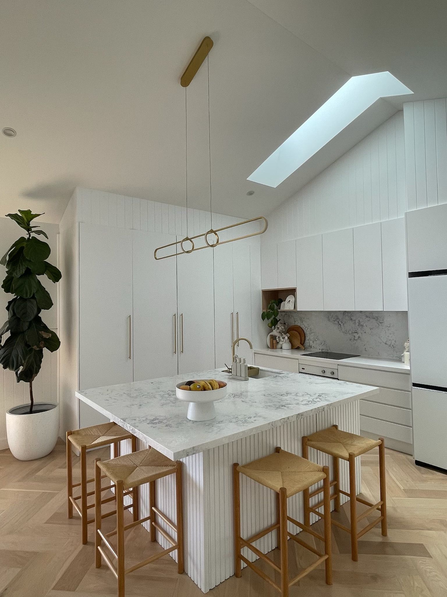 White kitchen with island, marble countertop, wooden stools, and skylight. — Hallam & Sons in Beard, ACT