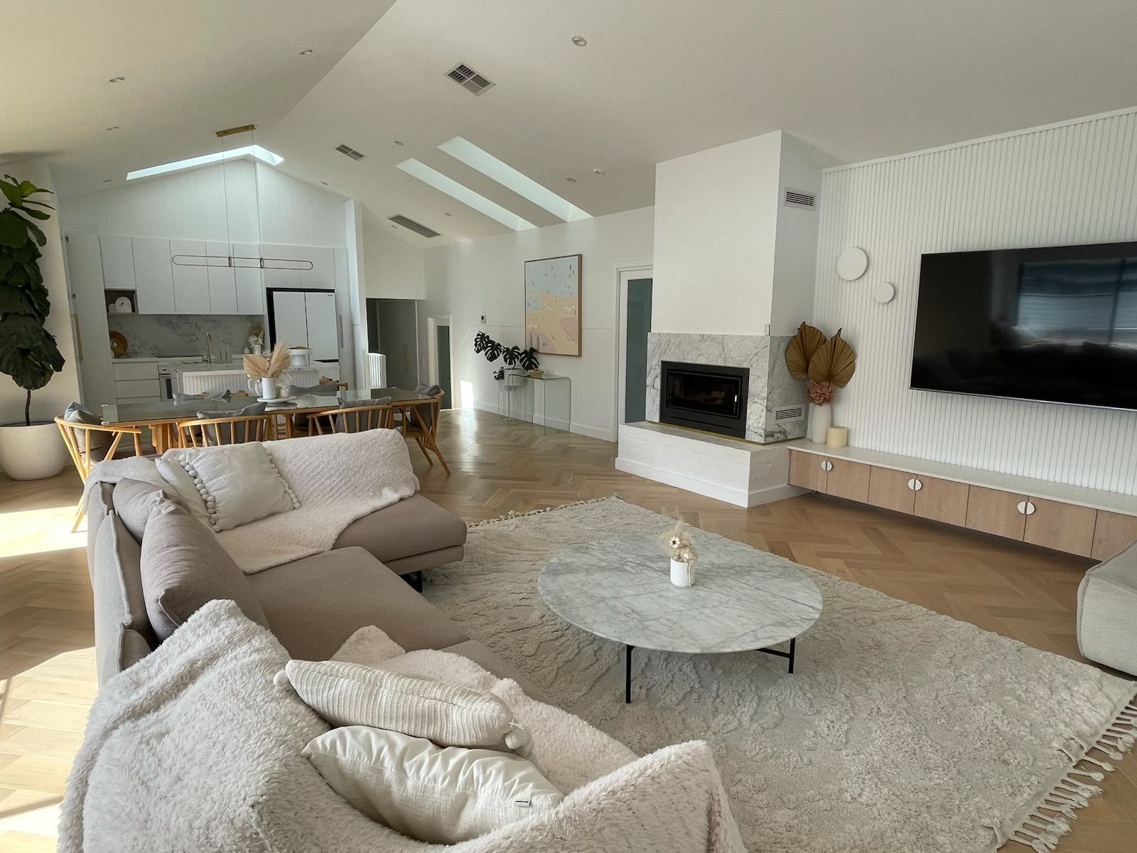 Spacious modern living room with neutral colours, vaulted ceilings, fireplace, and large TV. — Hallam & Sons in Beard, ACT