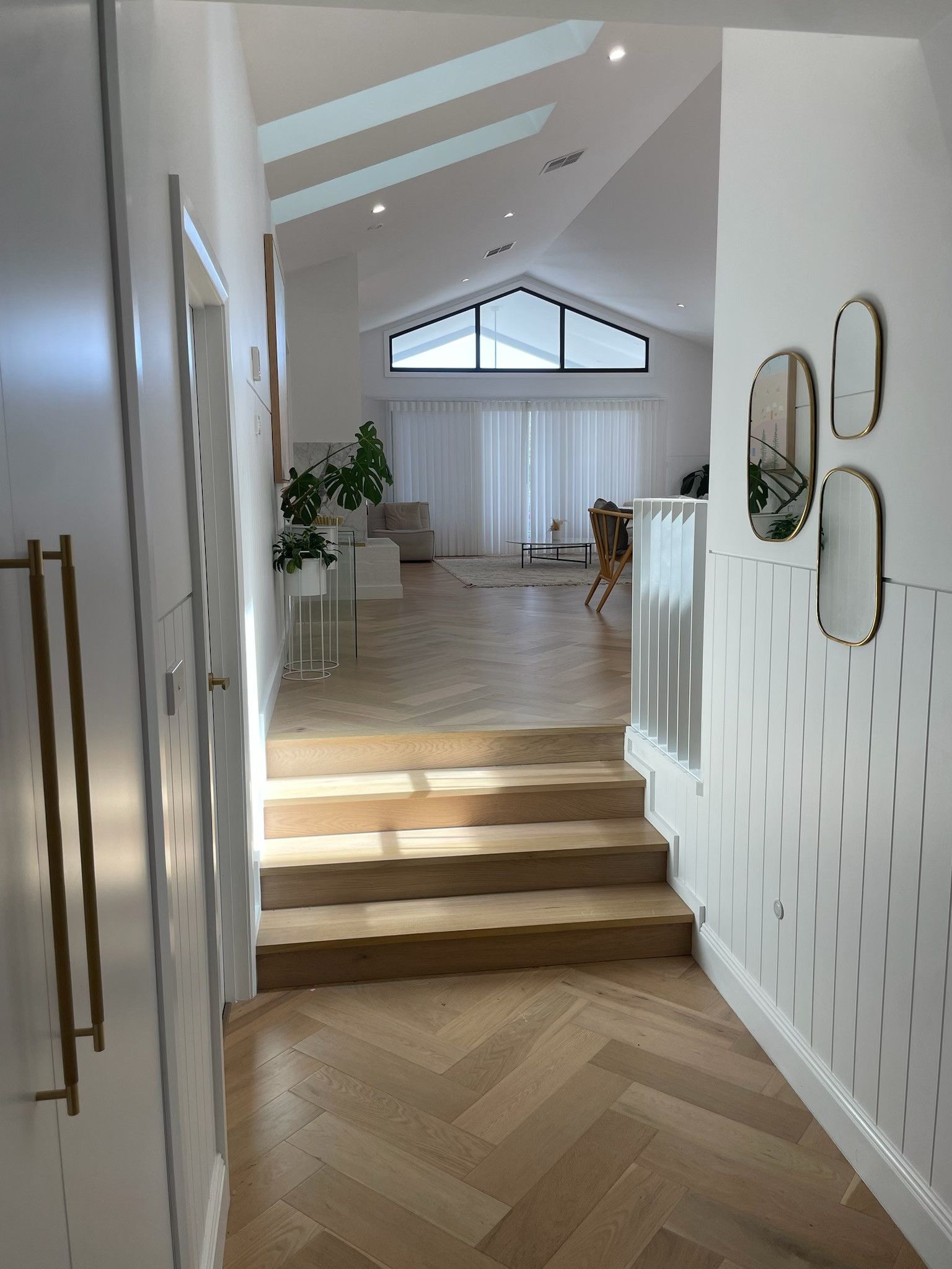 Hallway with wooden steps leading to a bright living room. Herringbone floors, white walls, decorative mirrors. — Hallam & Sons in Beard, ACT