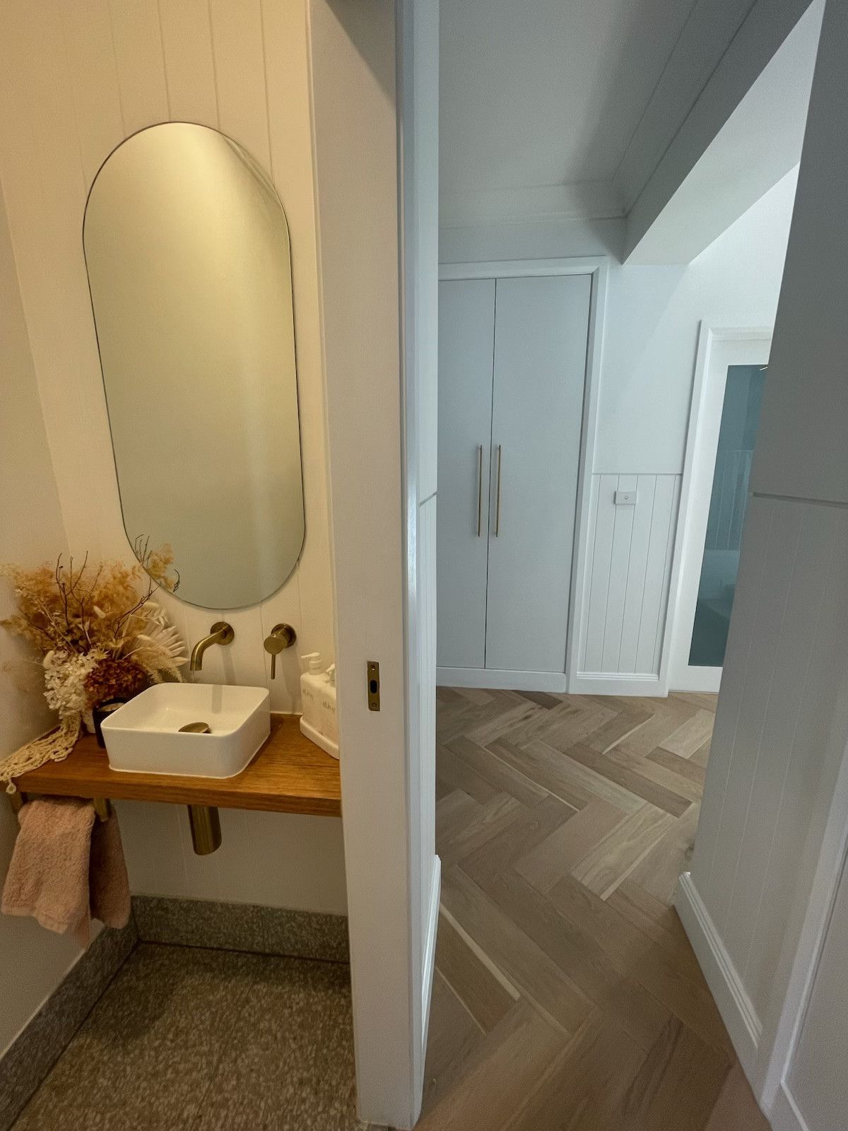 Bathroom with wood floor, white walls, sink, mirror, and a glimpse into a hallway with a closet. — Hallam & Sons in Beard, ACT