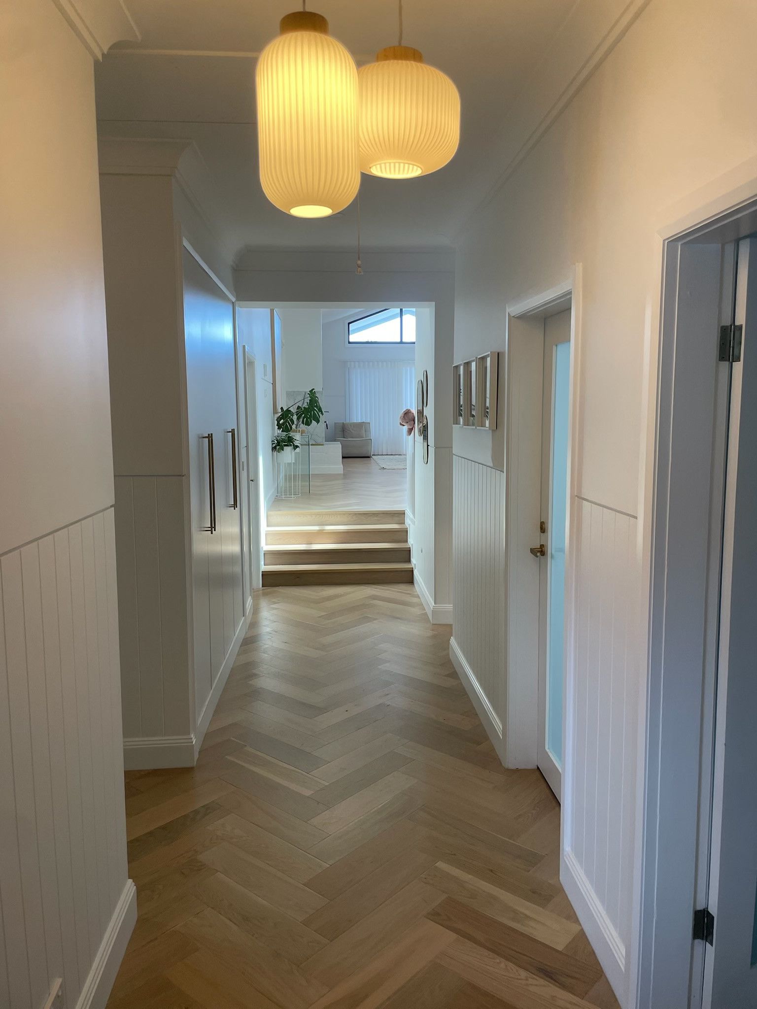 Narrow hallway with wooden herringbone floors, white walls, and two hanging globe lights. — Hallam & Sons in Beard, ACT
