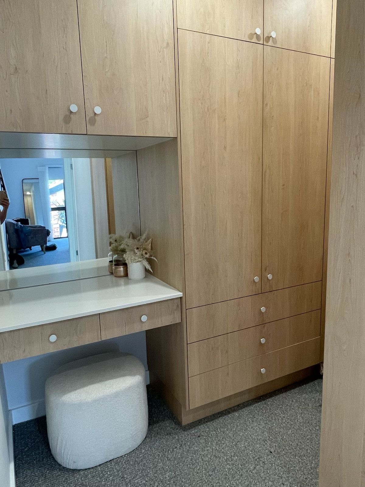 Built-in light wood vanity and closet with round knobs. A fluffy white stool sits beneath the vanity. — Hallam & Sons in Beard, ACT