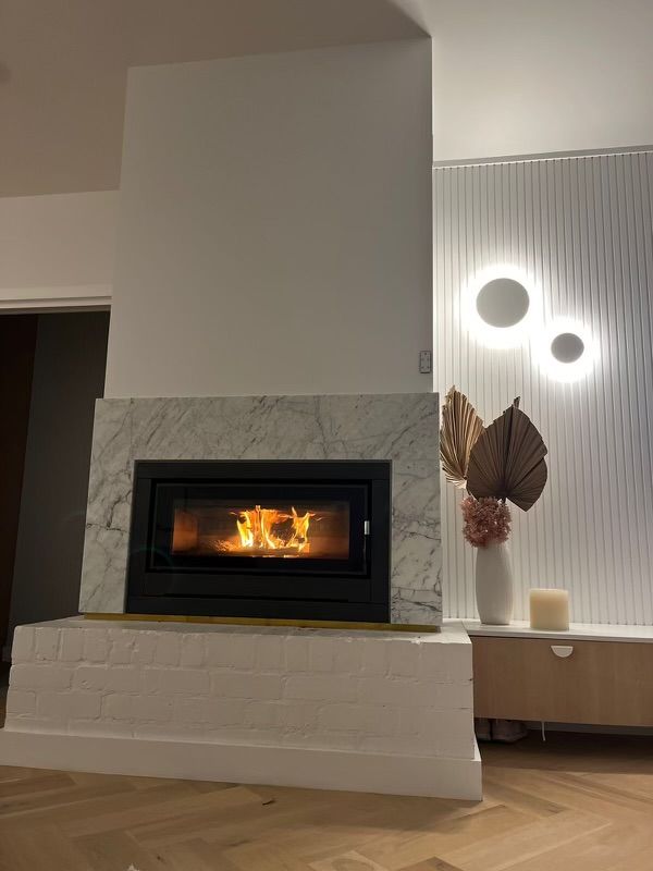 Fireplace with marble surround, flames burning, modern design with decorative wall lights and vase. — Hallam & Sons in Beard, ACT