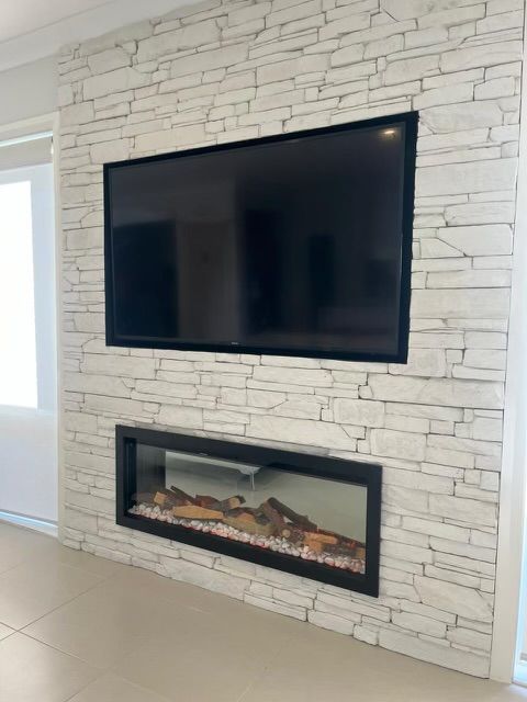 Television mounted above a fireplace on a white stone accent wall. — Hallam & Sons in Beard, ACT