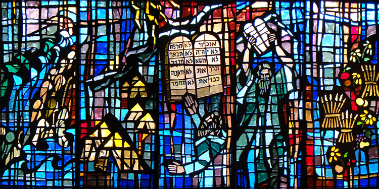 A stained glass window in a church shows a man holding a book.