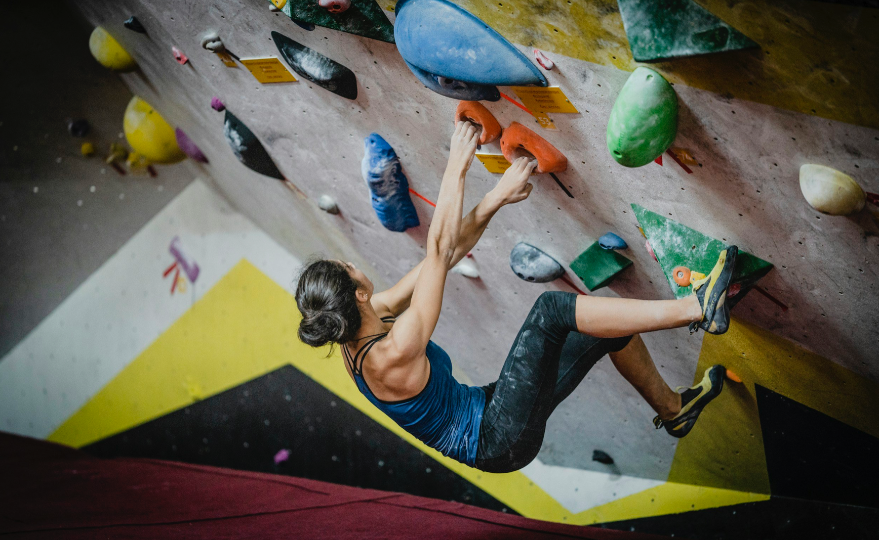 A woman is climbing a climbing wall in a gym.