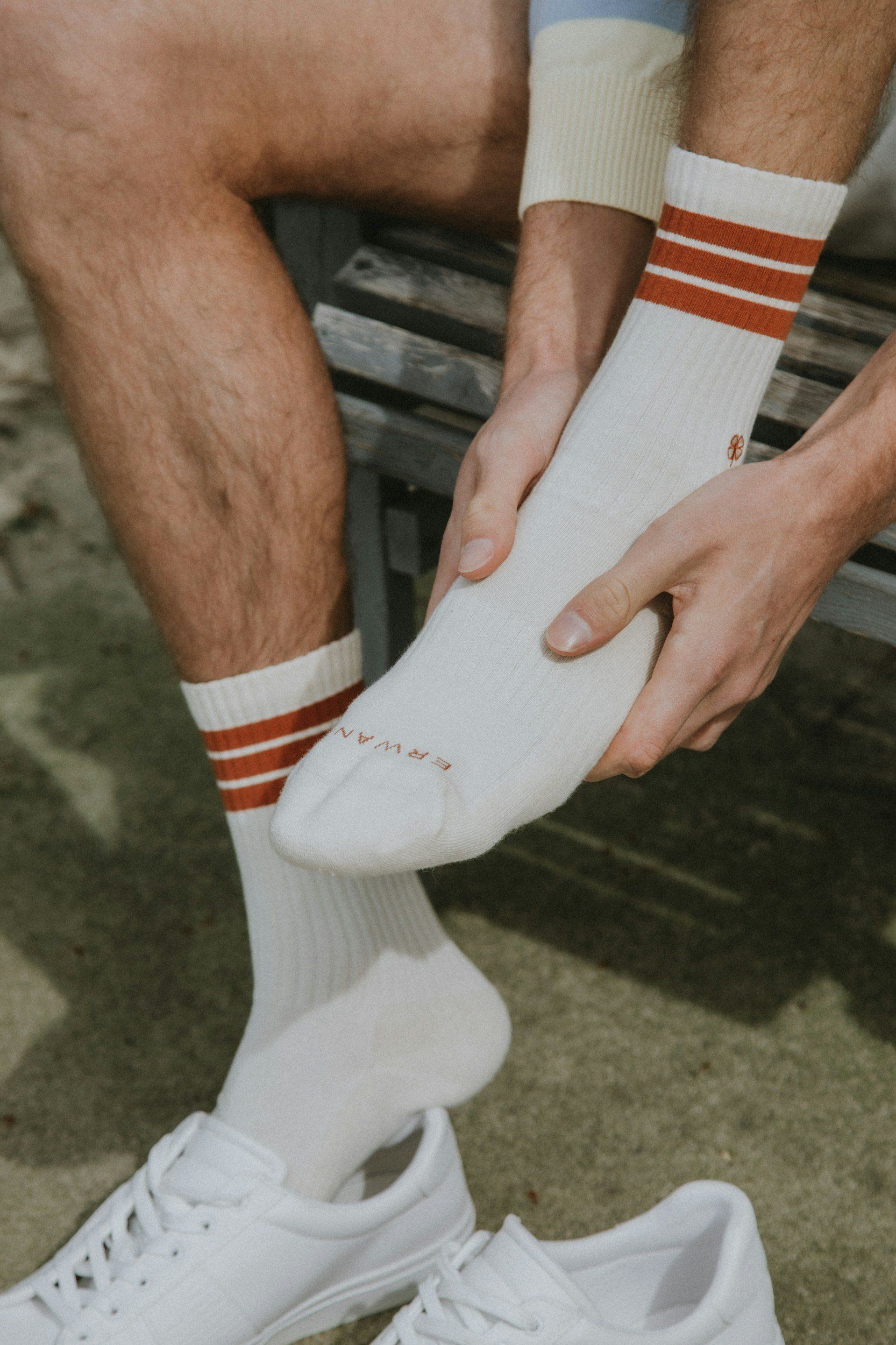 A person is putting on a pair of white socks with red stripes.