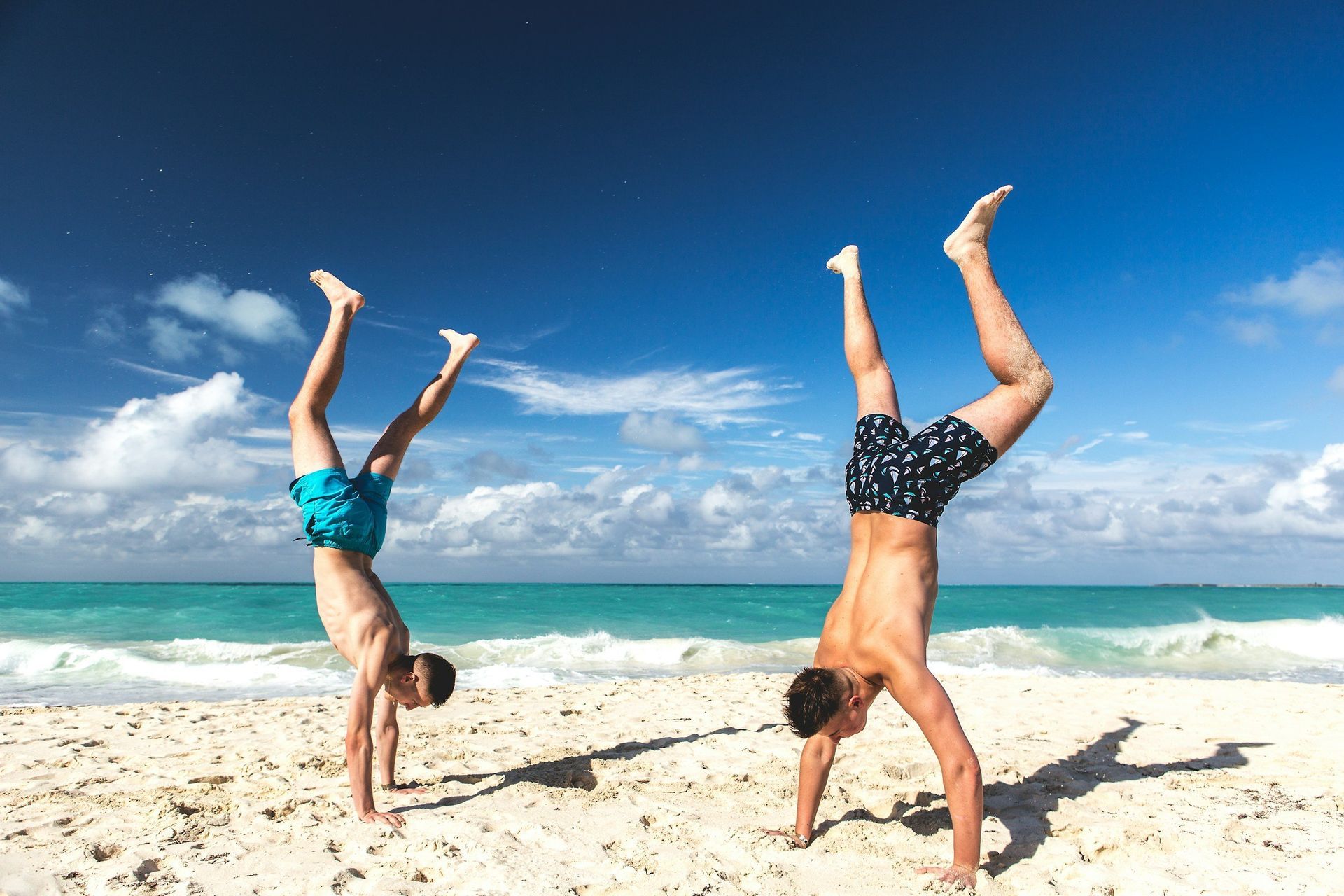 Two men are doing handstands on the beach.