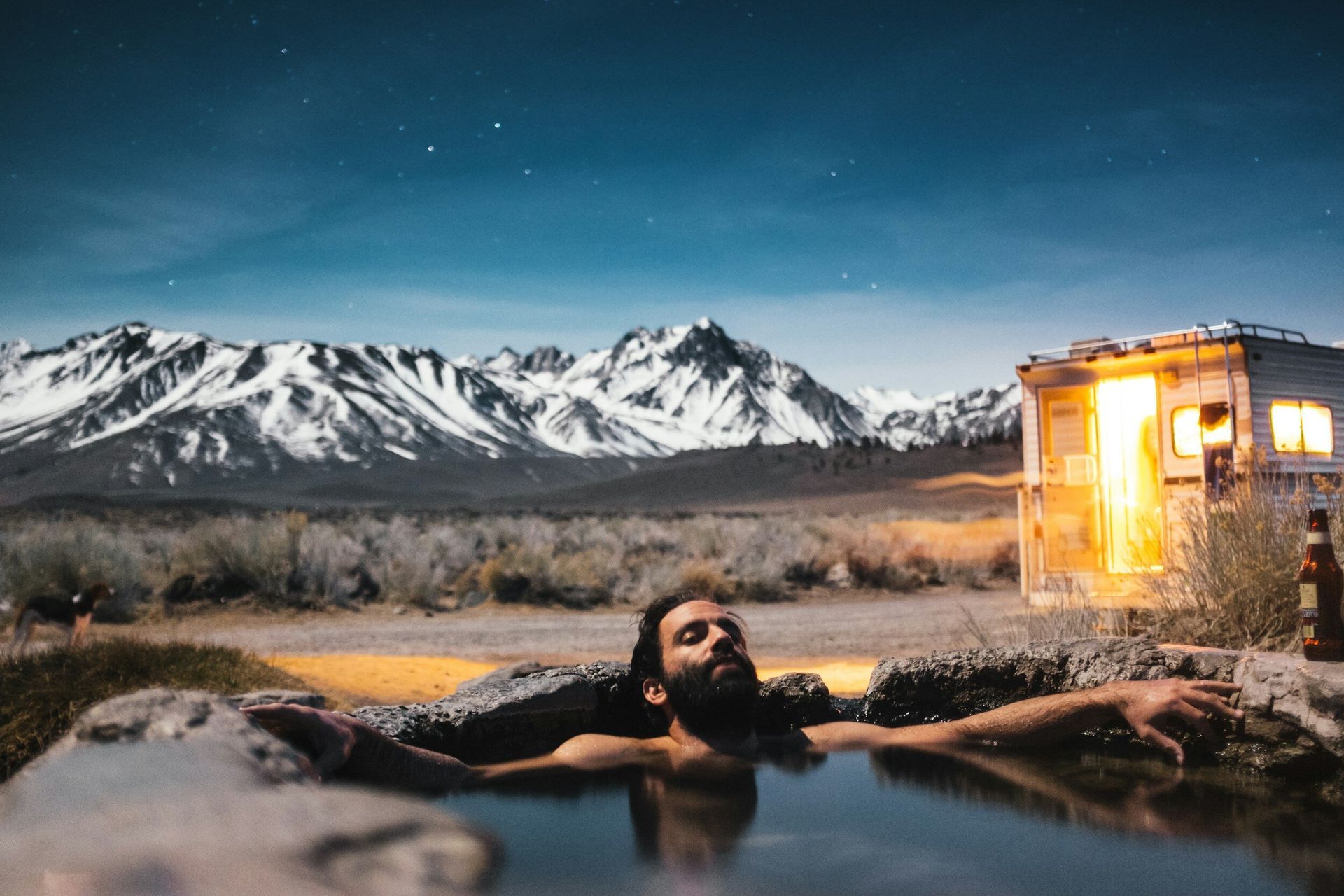 A man is laying in a hot tub with mountains in the background.