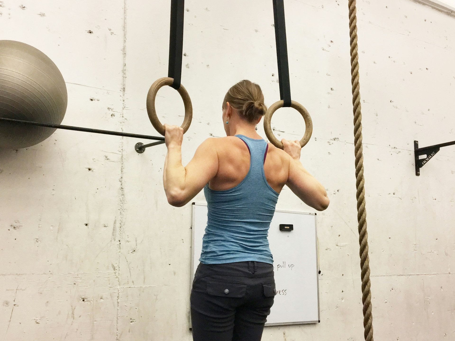 A woman is doing pull ups on gymnastic rings in a gym.