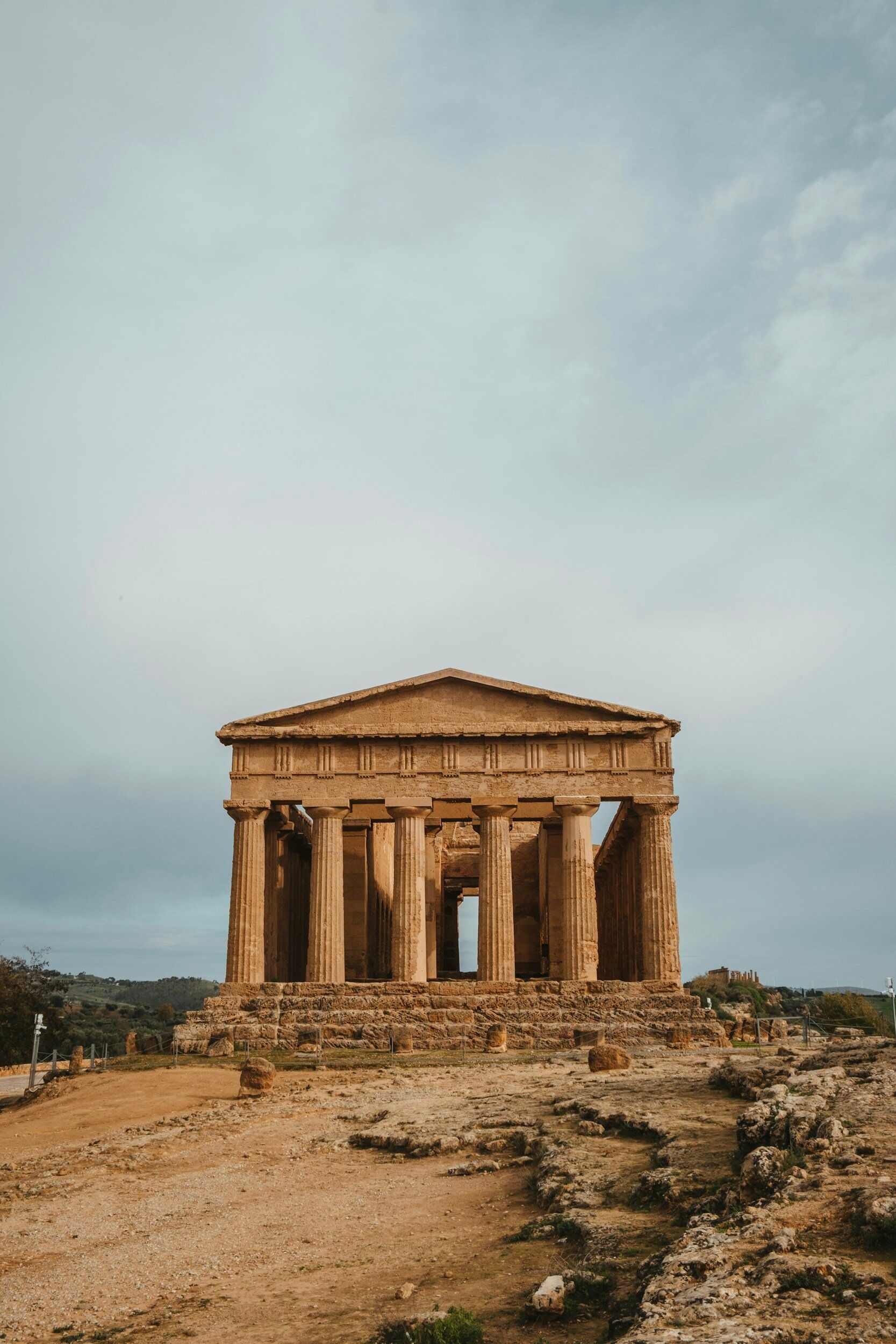 A large stone building with columns is sitting on top of a dirt hill.