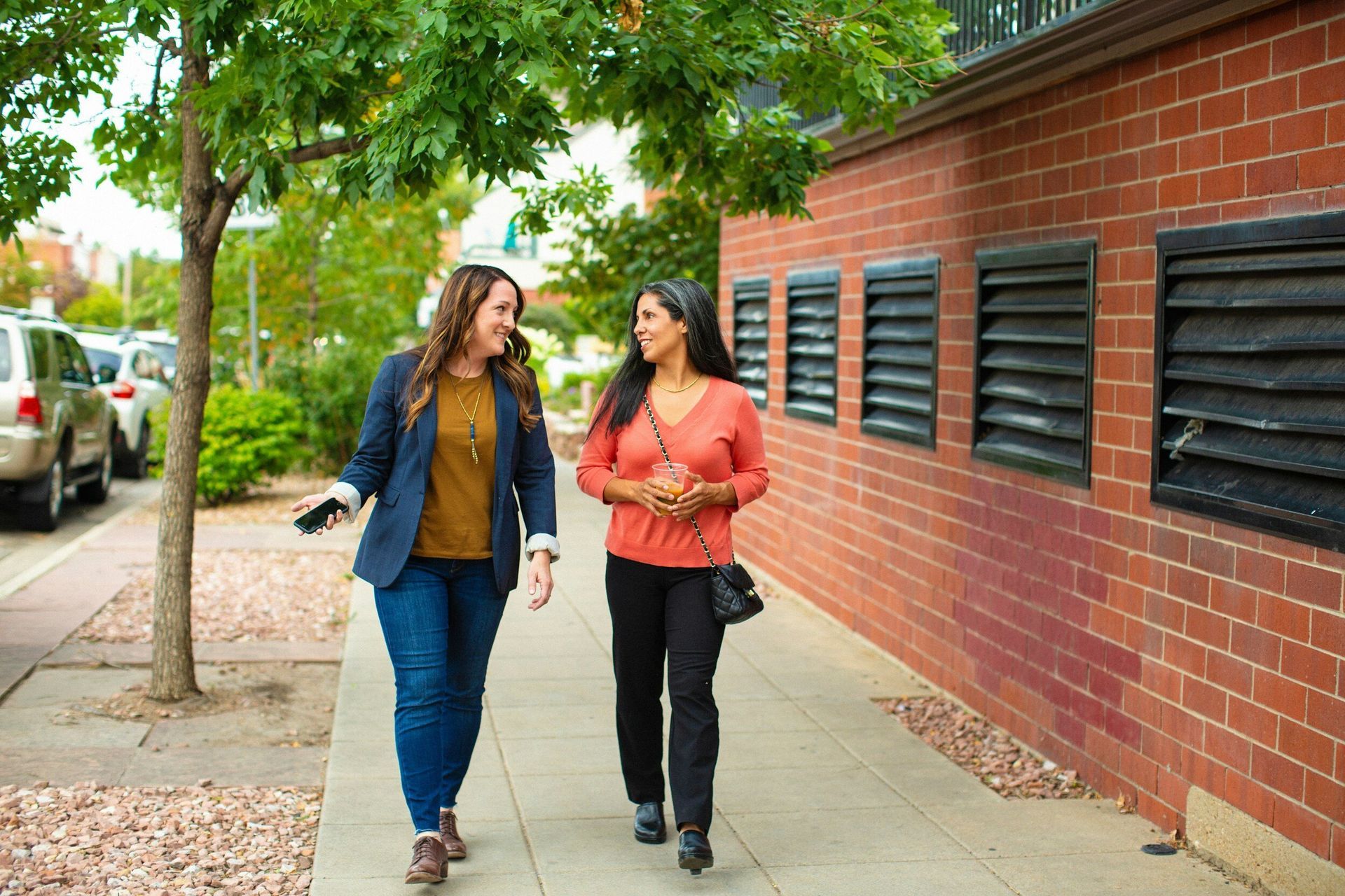Two women are walking down a sidewalk in front of a brick building.