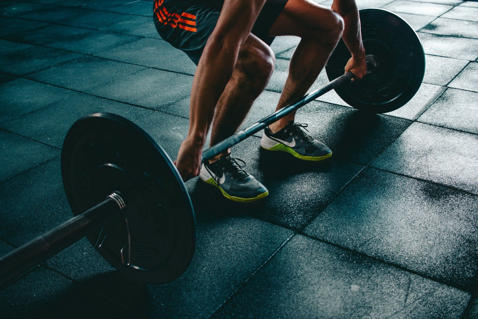 A man is squatting down to lift a barbell in a gym.
