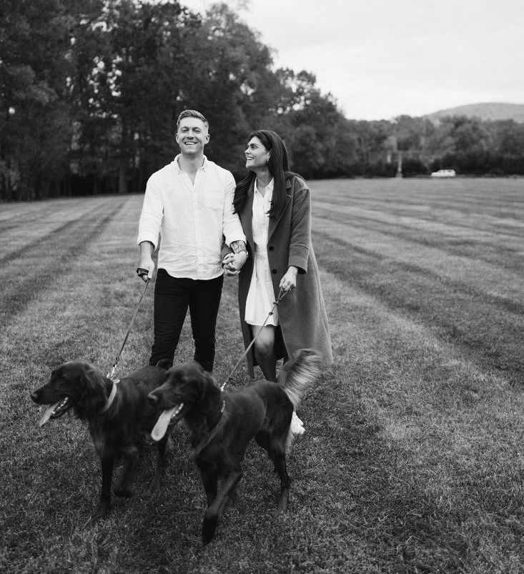 A man and a woman are walking their dogs in a field.