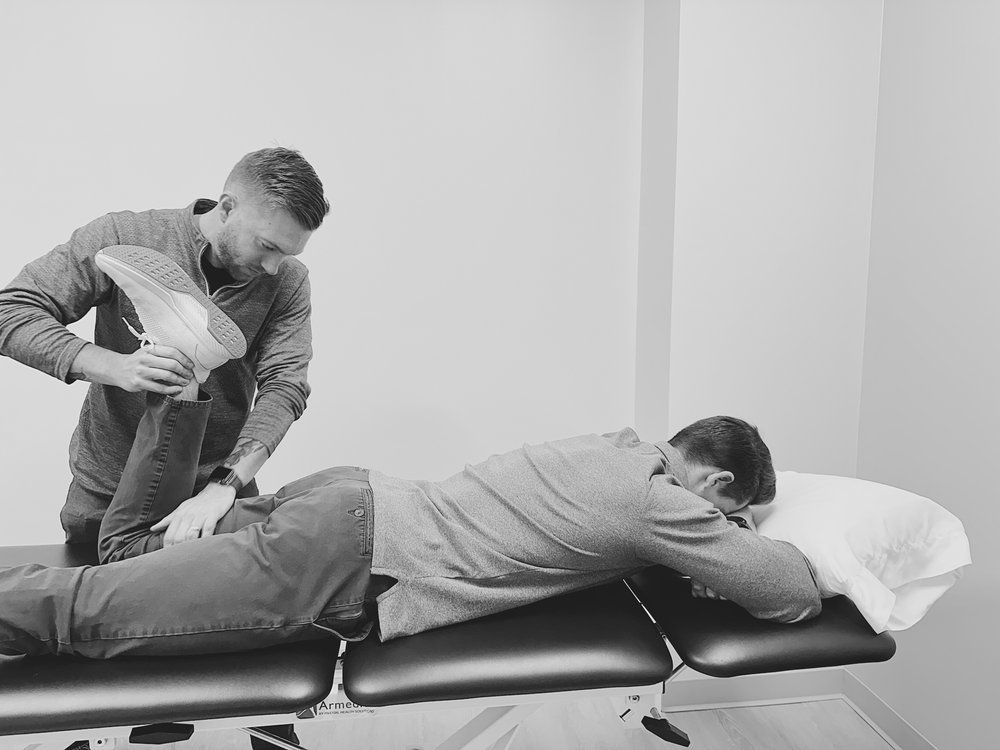 A man is laying on a table while another man stretches his leg.