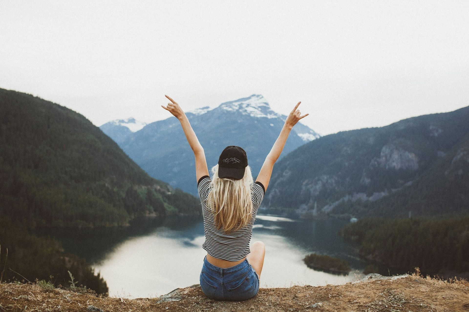 A woman is sitting on top of a mountain with her arms in the air.