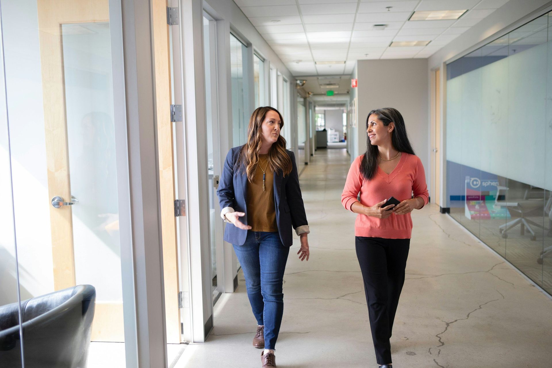 Two women are walking down a hallway in an office building.