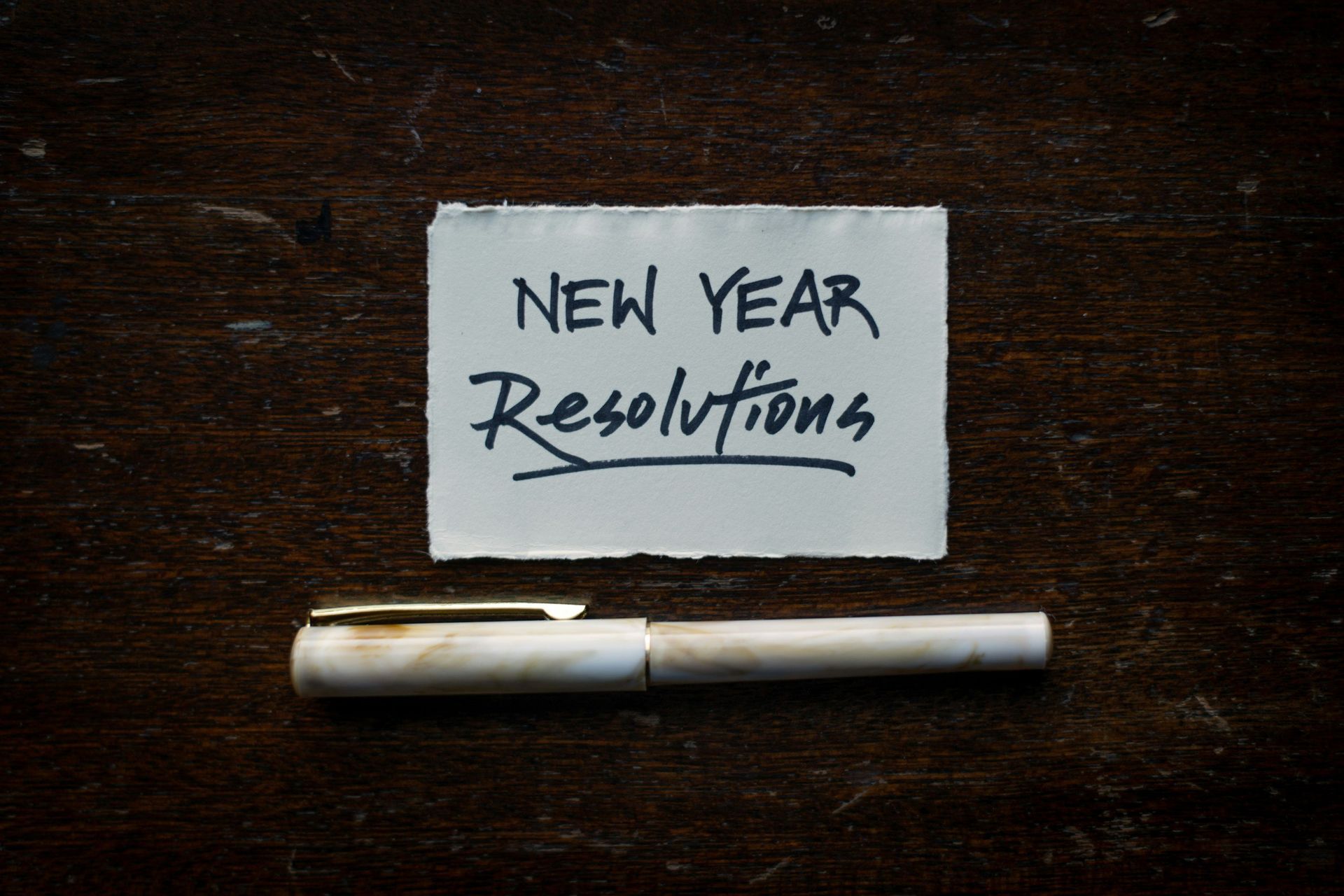 A pen is sitting next to a piece of paper that says new year resolutions.