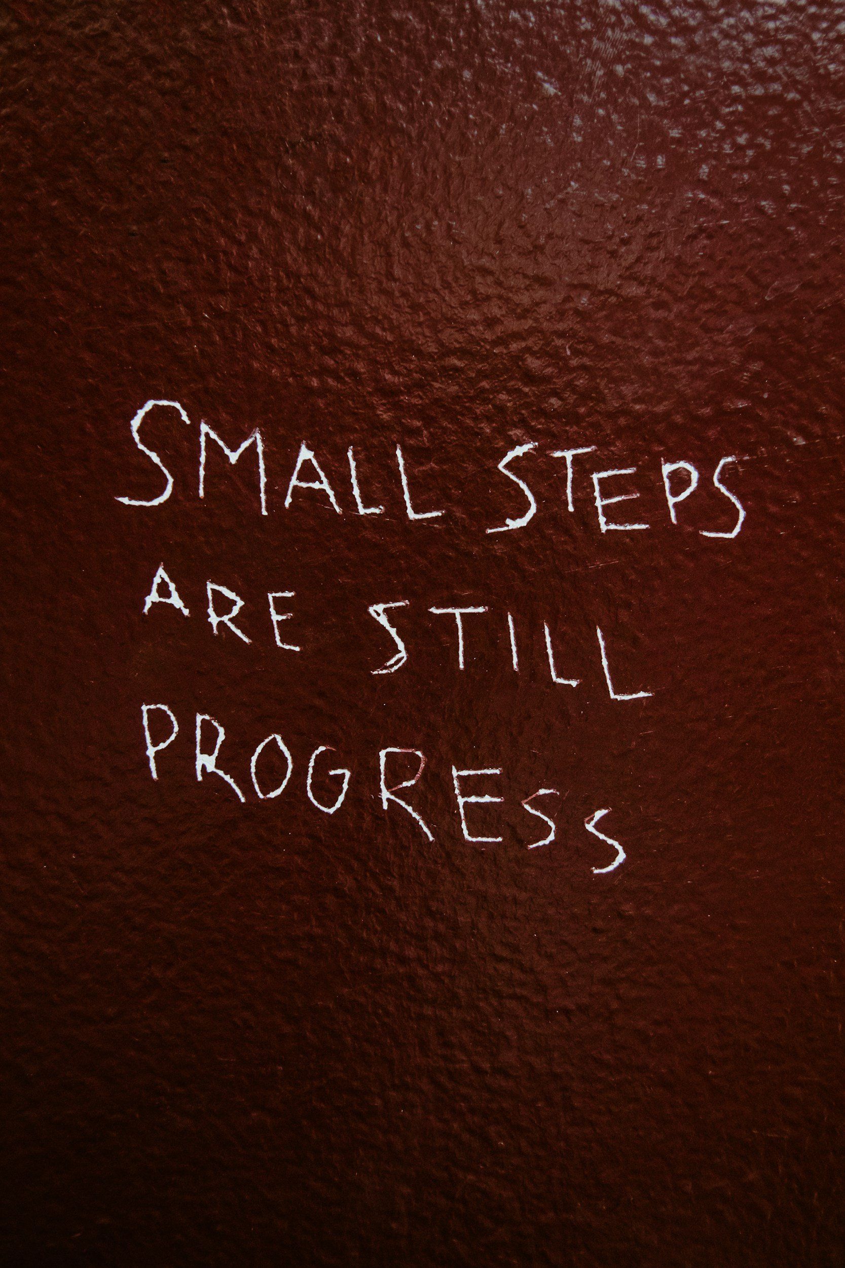 Small steps are still progress written on a brown wall