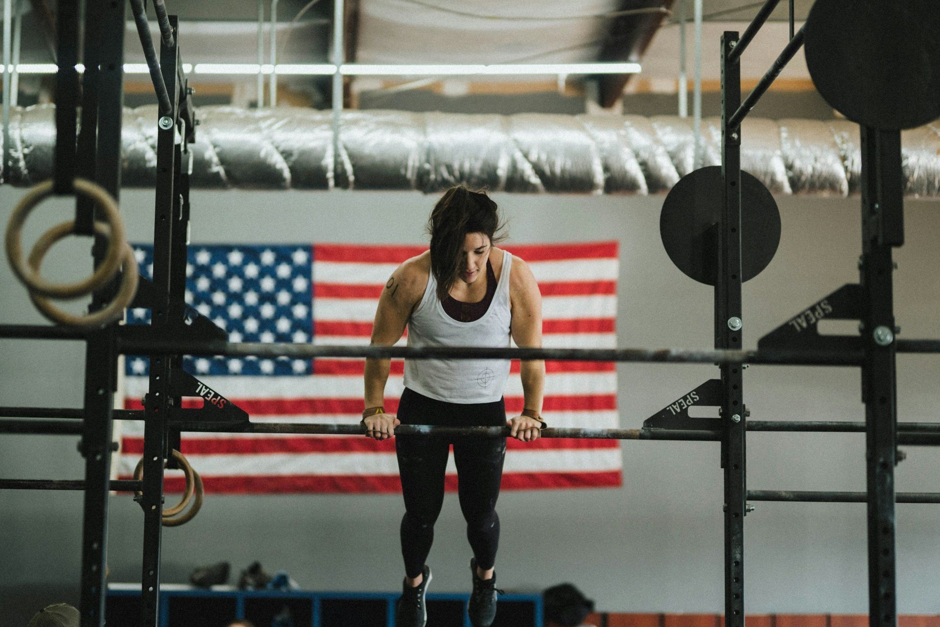 A woman is lifting a barbell in a gym in front of an american flag.