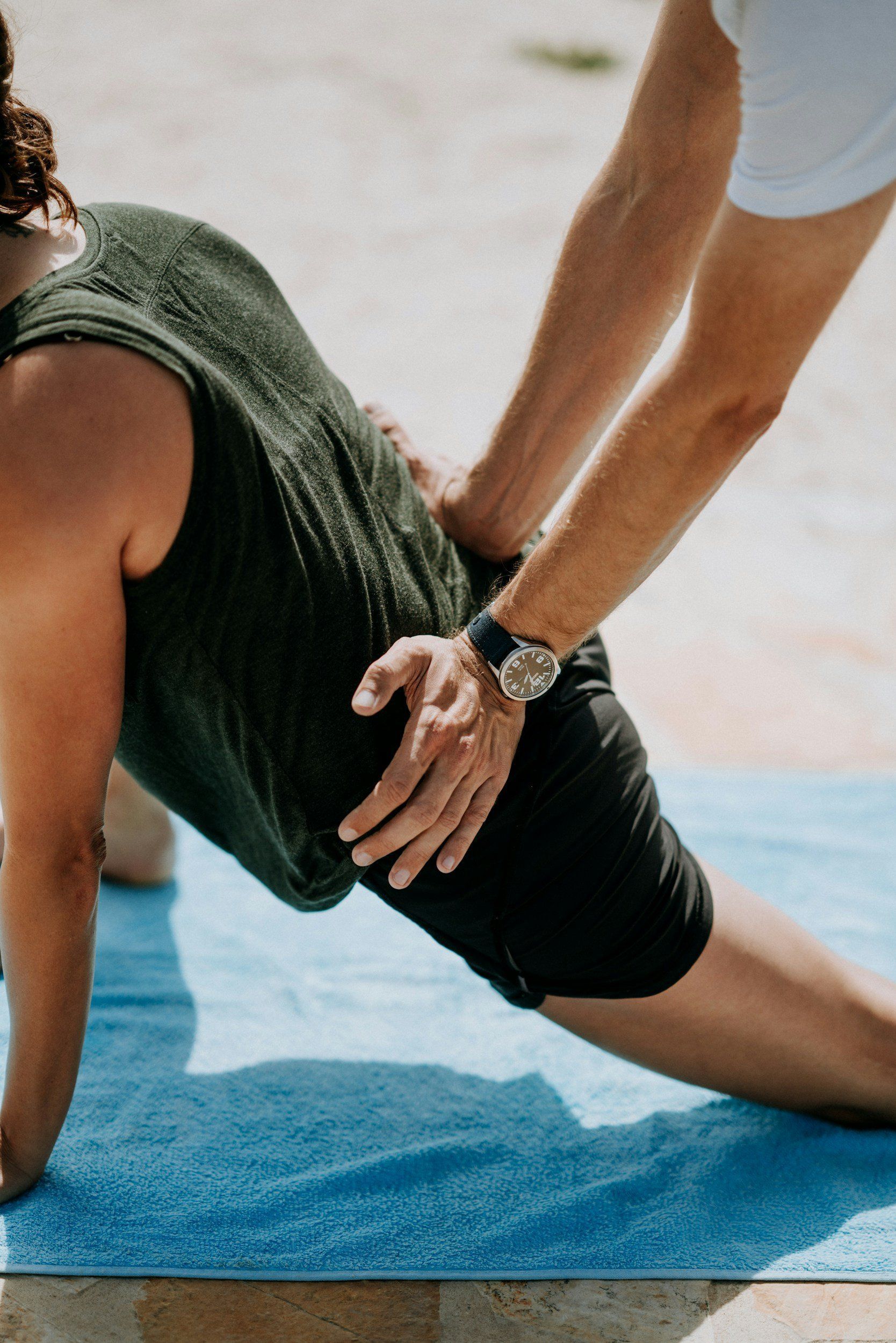 A man is helping a woman stretch her legs on a yoga mat.