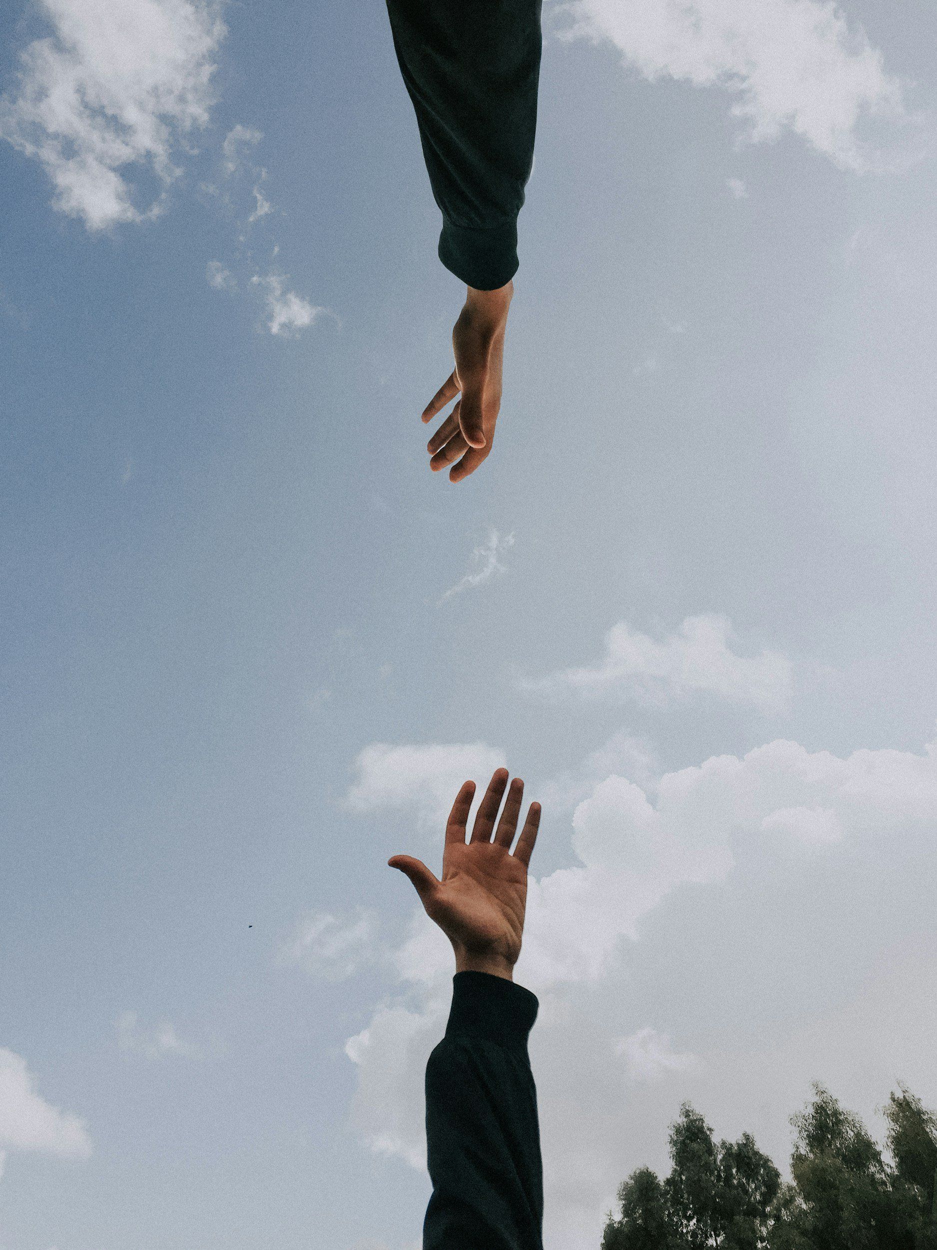 Two hands are reaching out towards each other in the sky.