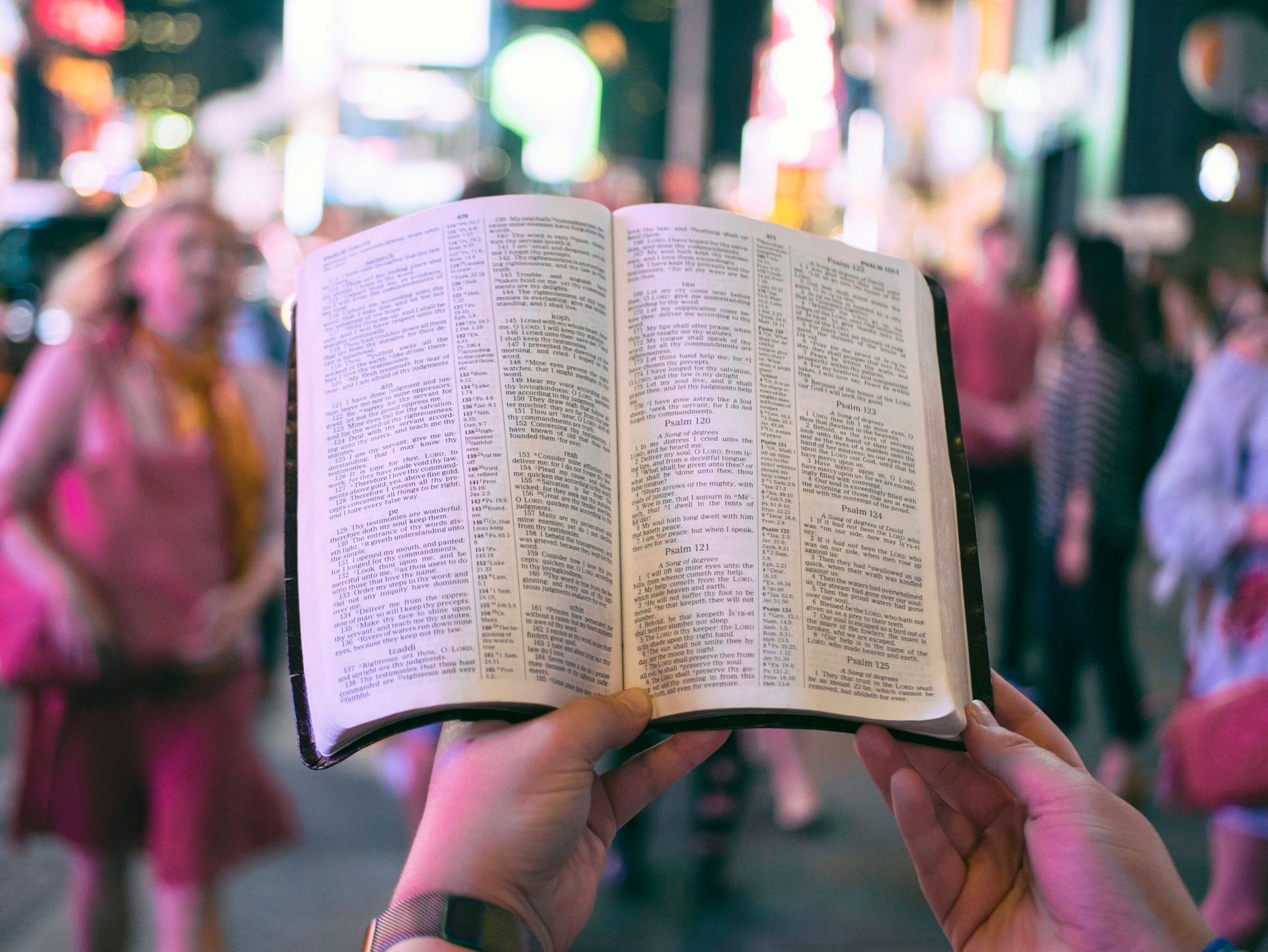 A person is holding an open bible in front of a crowd of people.