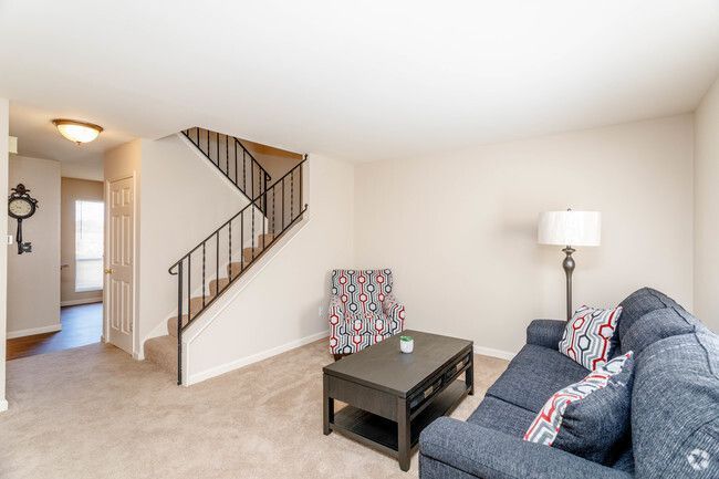 A living room with a couch , chair , coffee table and stairs.