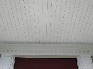 The ceiling of a porch with a red door and white trim.
