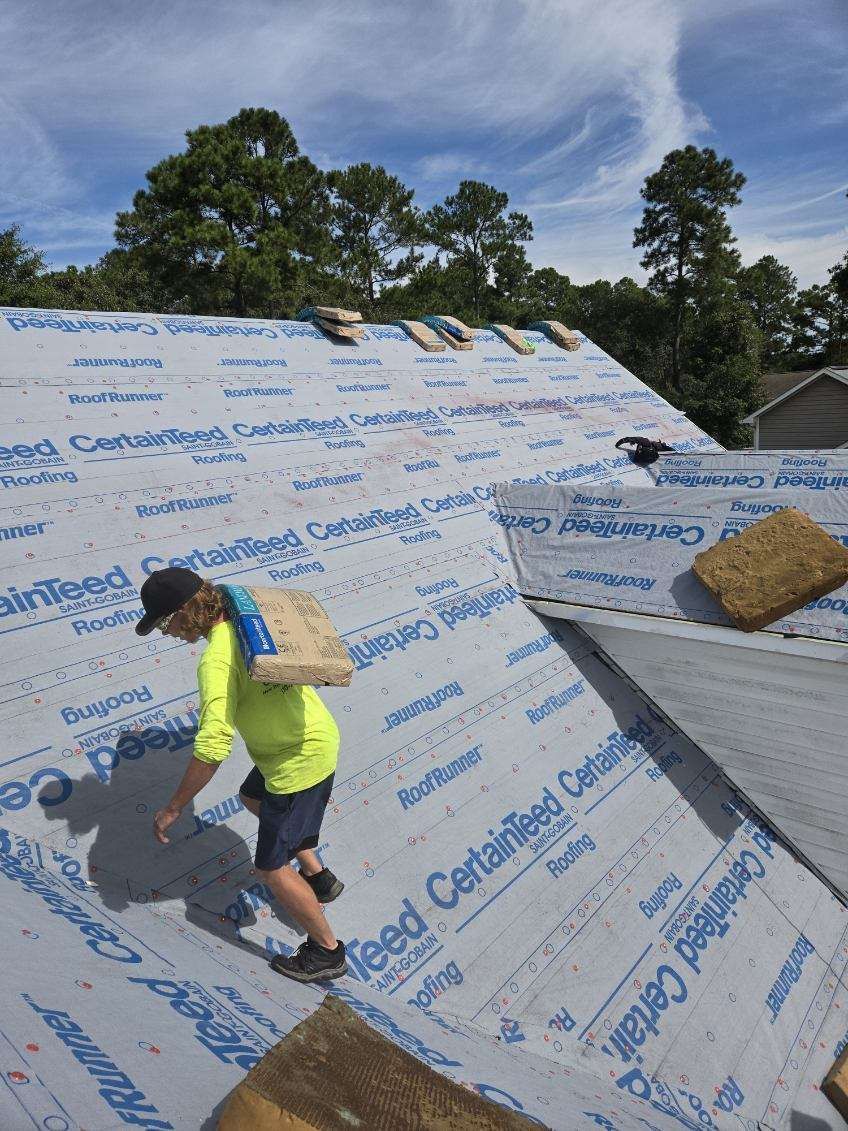 A man is standing on top of a roof with a bag on his back — Jacksonville, NC — JW Roofing & Exteriors