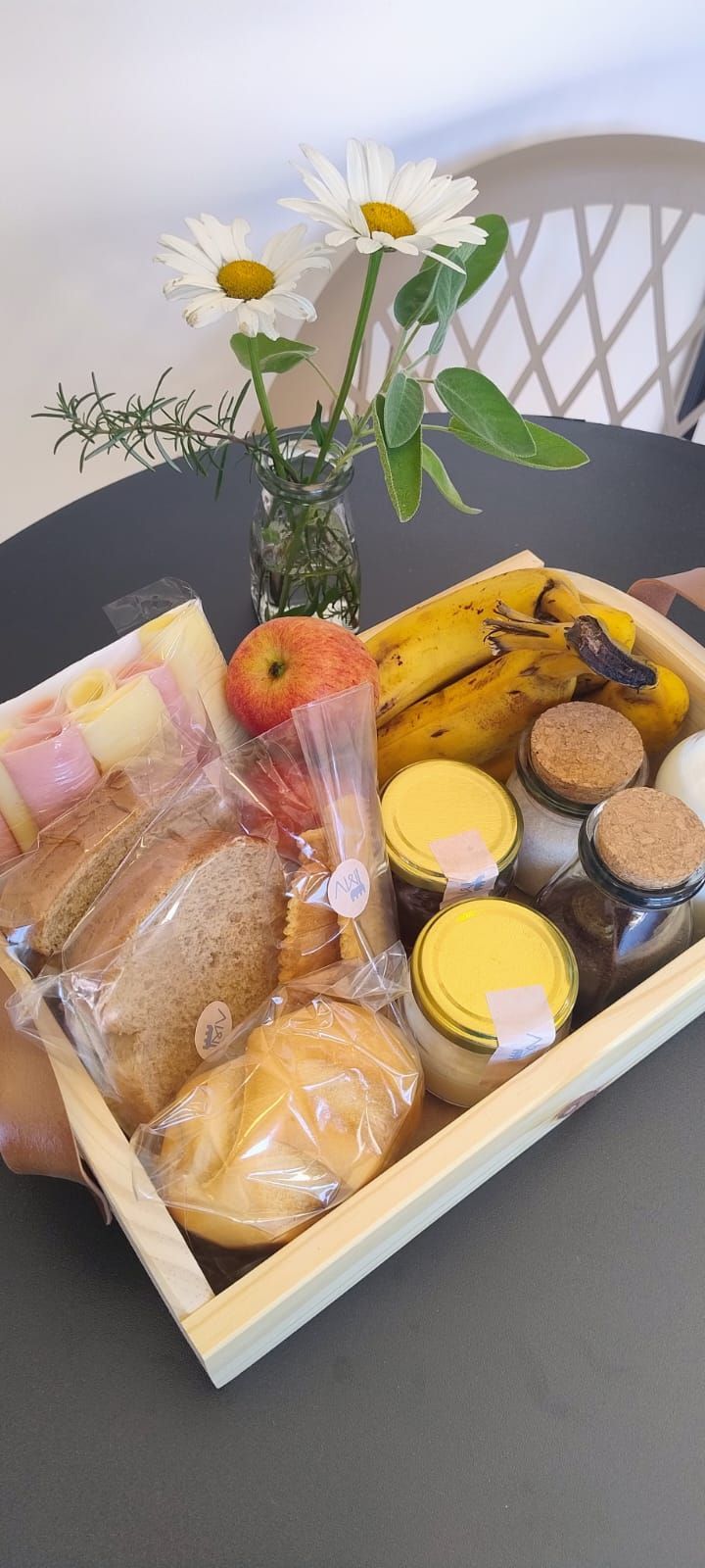 Cesta de café da manhã com diversos alimentos, incluindo pão, frutas e itens embalados.