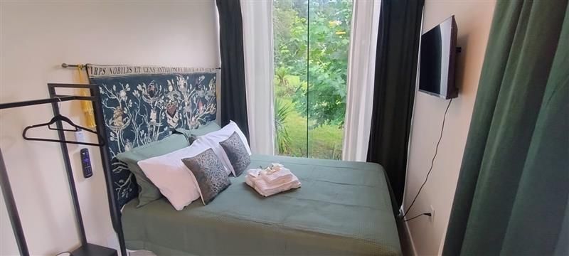 Quarto de hotel pequeno com cama, mesa de jantar pequena, TV, frigobar e prateleiras para guardar coisas.