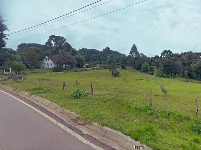 Campo gramado com uma casa em uma colina, à beira de uma estrada, sob um céu nublado.