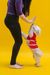 A woman is standing next to a small white dog wearing a red dress.
