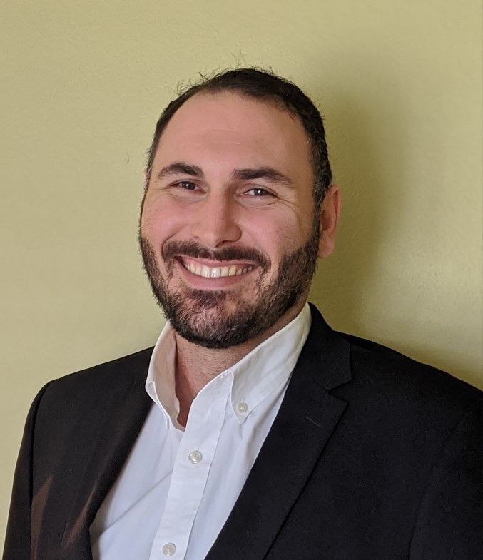 A man with a beard is wearing a suit and smiling for the camera.