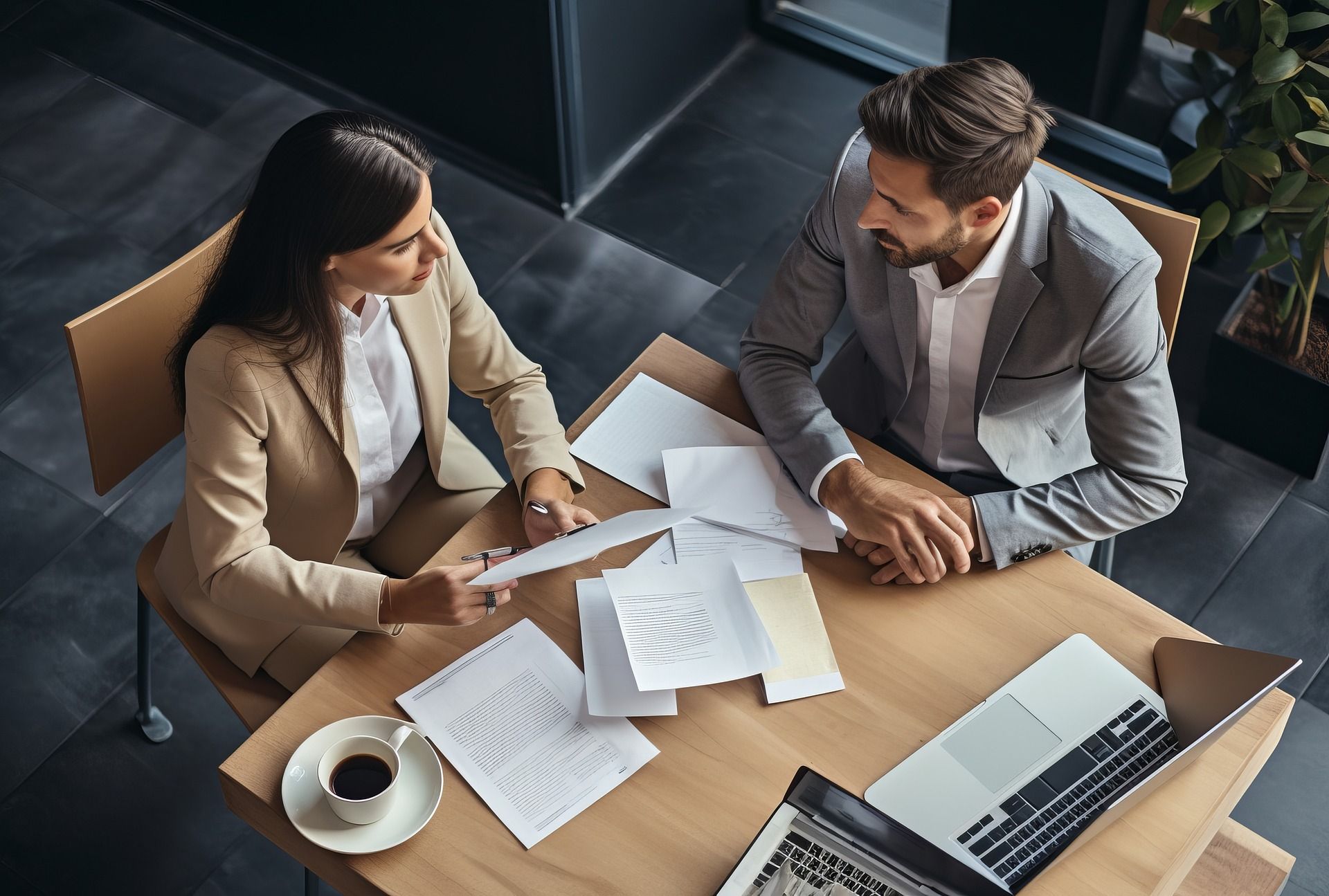 A man and a woman are sitting at a table with papers and a laptop.