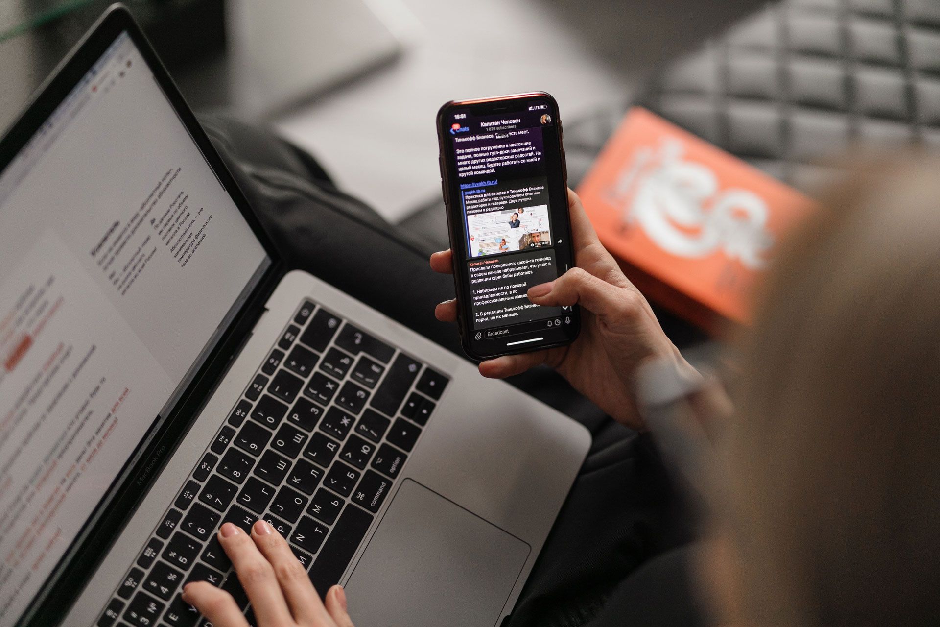 A person is holding a cell phone in front of a laptop computer.
