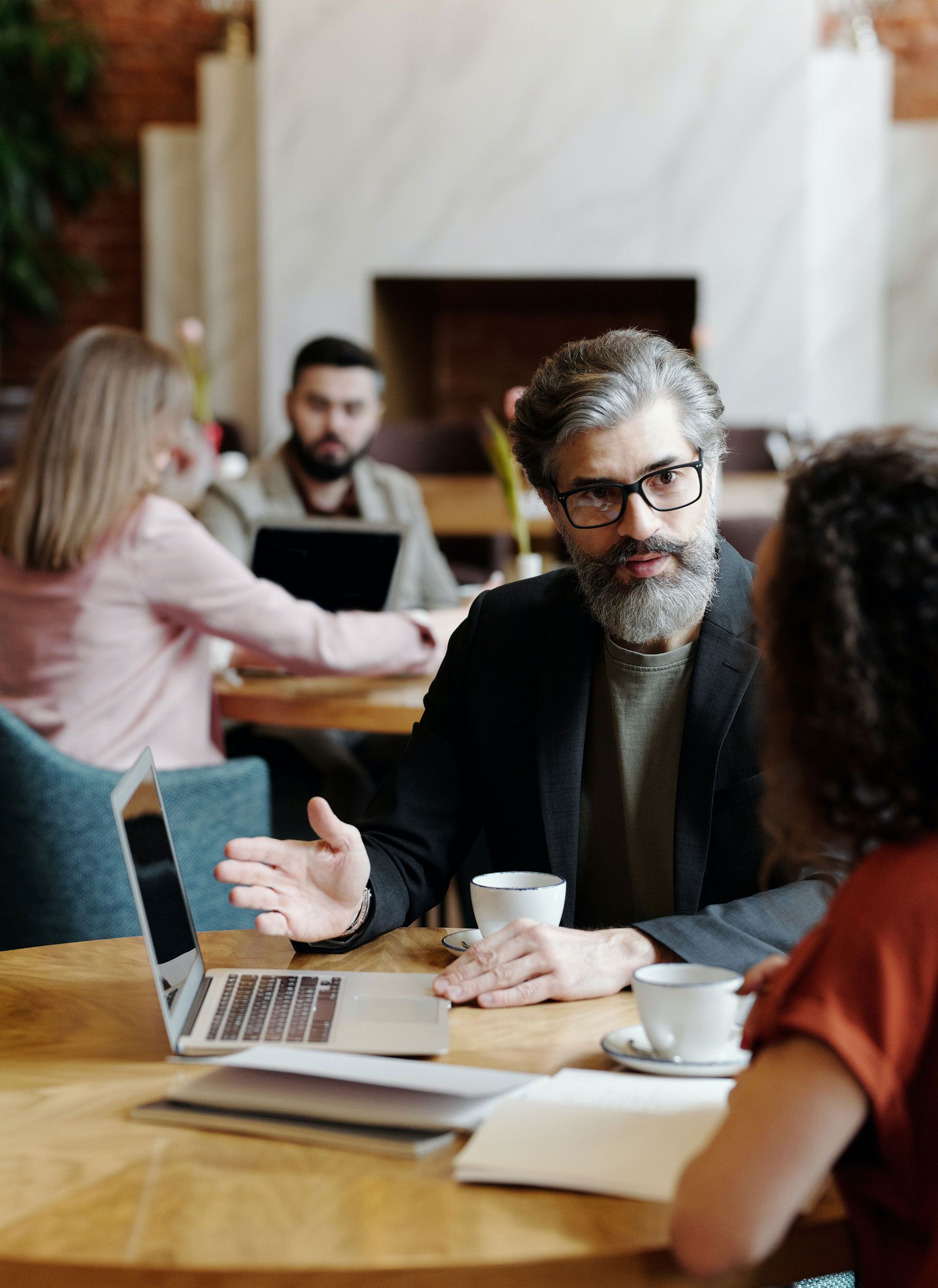 A man with a beard is sitting at a table talking to a woman.