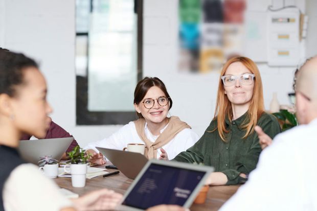 A group of people are sitting around a table with laptops.