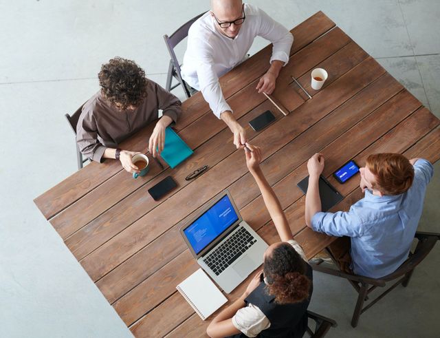 A group of people are sitting around a wooden table with laptops.
